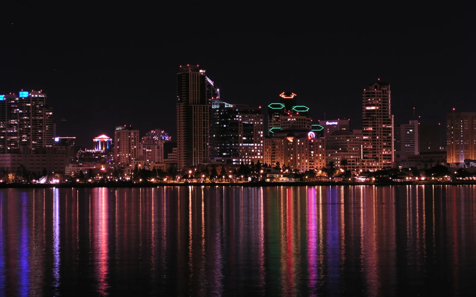 The downtown San Diego skyline illuminated at night, with city lights reflecting off the bay waters and the silhouette of buildings against the evening sky